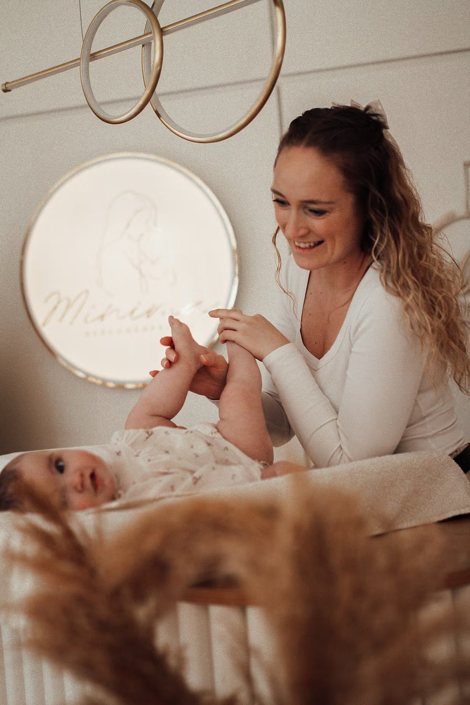 Julia spielt lächelnd mit einem Baby auf der Wickelkommode, im Hintergrund leuchtet das Minima-Logo