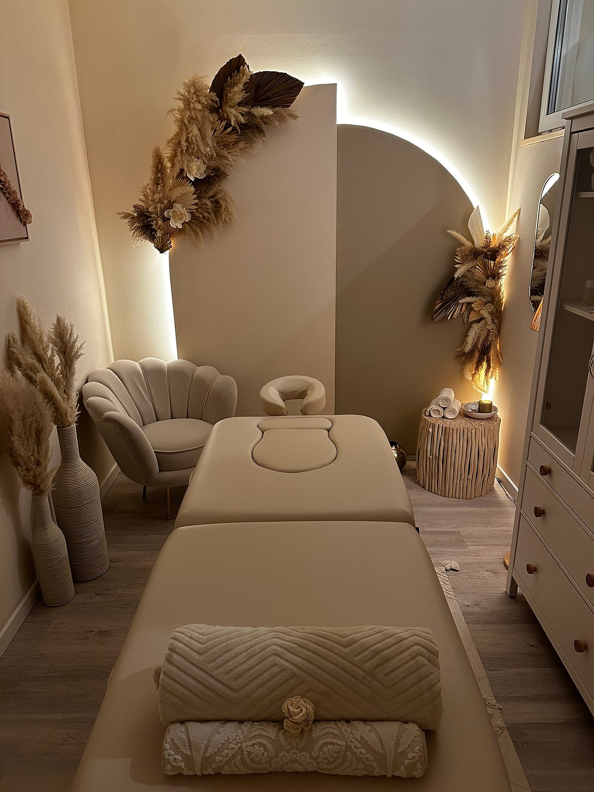 Der warm beleuchtete Massageraum der Praxis mit Liege, Trockenblumen und Bogenwand