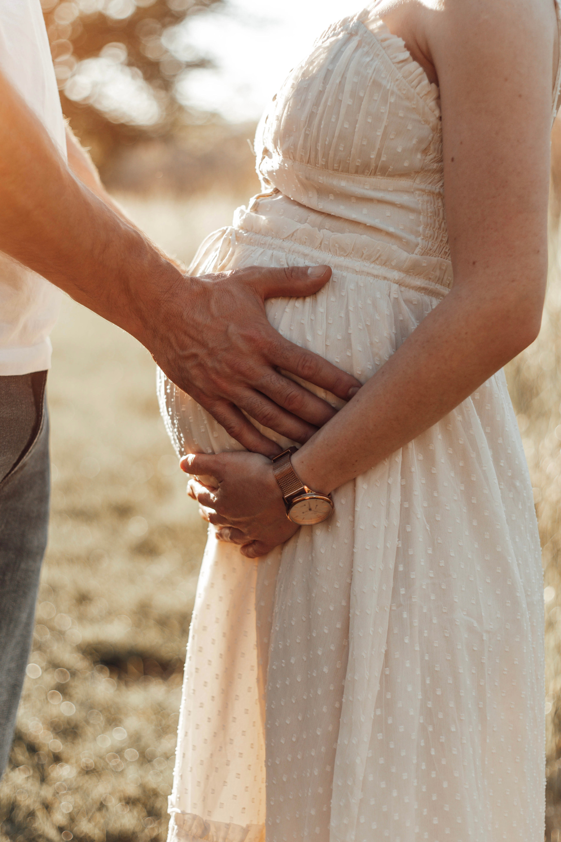 Ein Paar hält im warmen Abendlicht gemeinsam den Babybauch